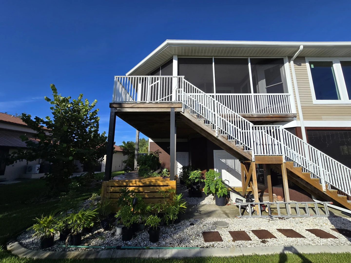 Elevated home with white balcony and stair railings, exterior siding and exposed timber below.