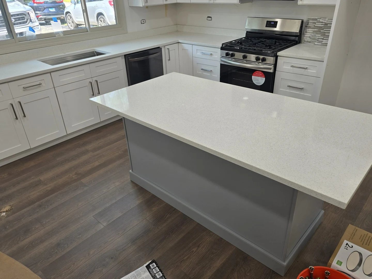 A pale kitchen island countertop with gray cabinetry and wood-look flooring.