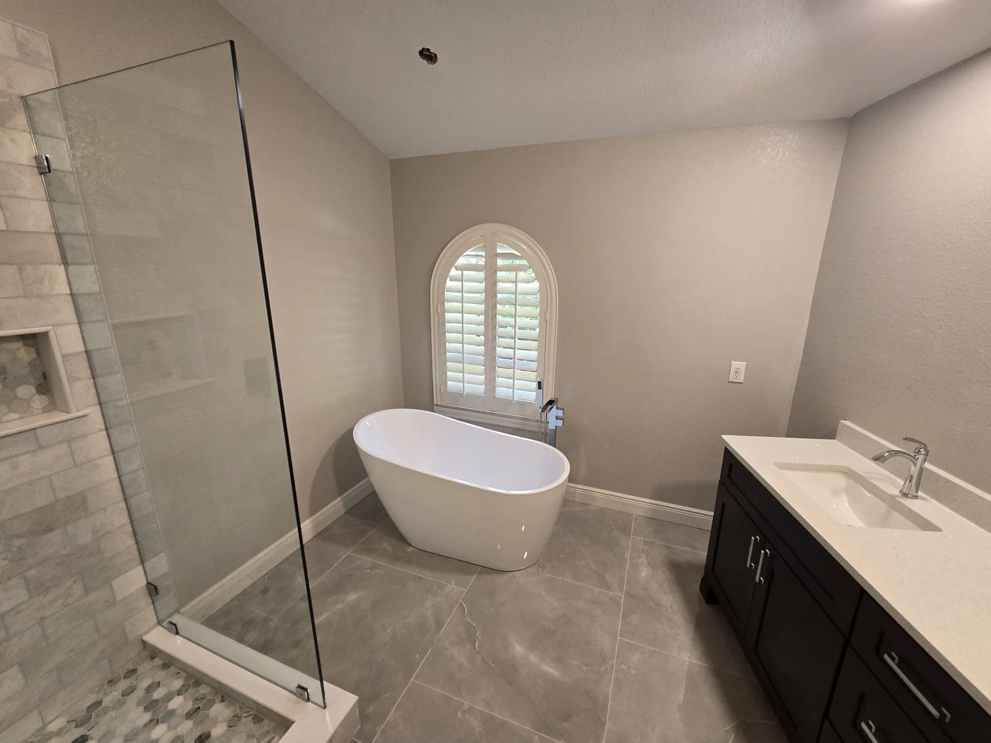 Freestanding white bathtub beneath an arched window beside a glass shower.