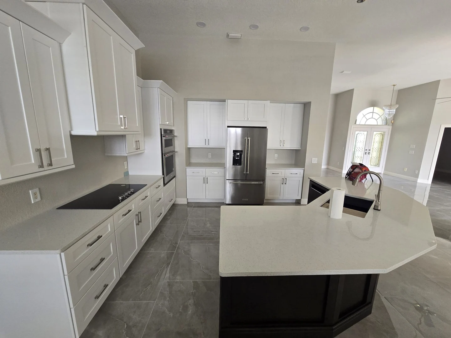 White kitchen cabinets, a dark island, pendant lighting and gray floor tiles.