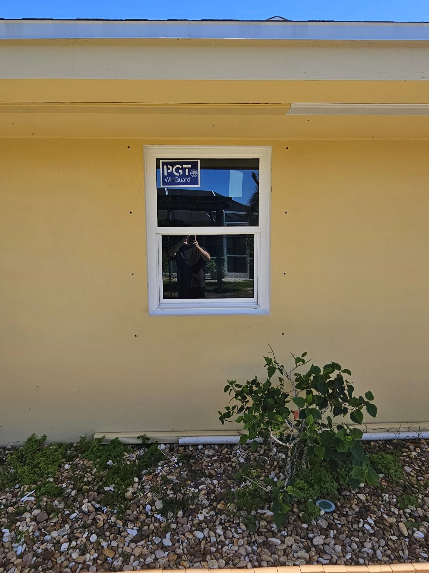 Stickered white-framed window on a yellow exterior wall during installation.