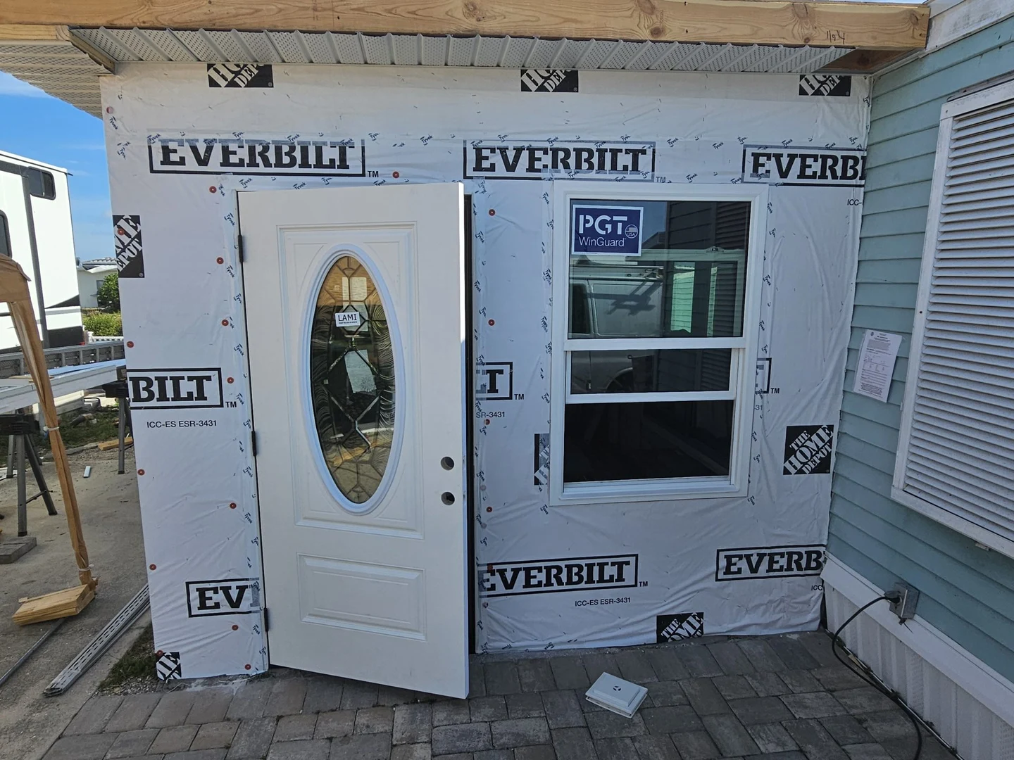 Open decorative-glass entry door beside a stickered window, with exterior finishes incomplete.