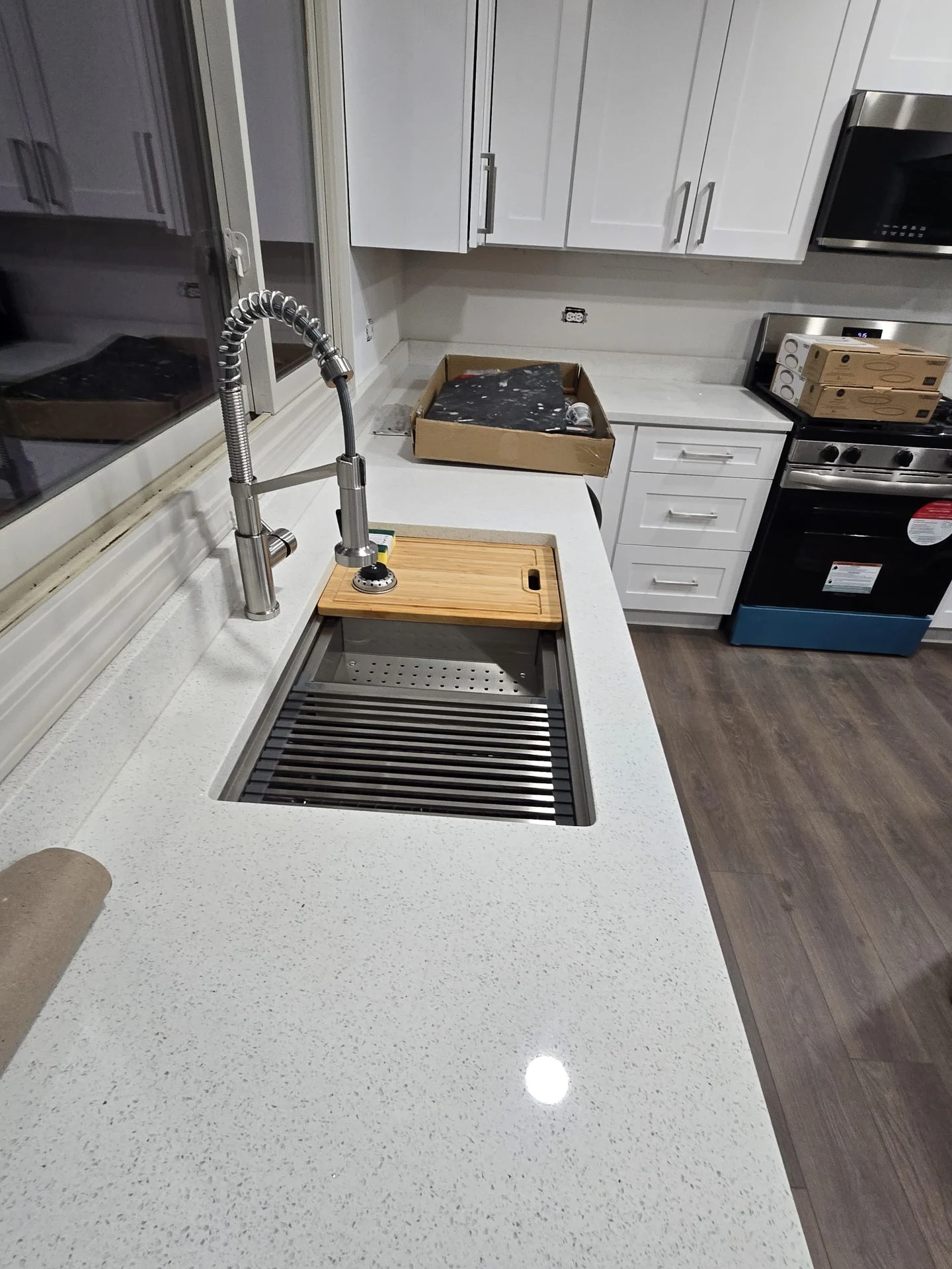 Kitchen counter and sink during installation, with white cabinetry, a tall faucet, protective packaging and unfinished outlet details.