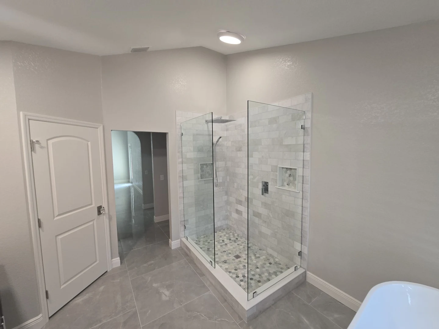 Bathroom with a glass shower enclosure, pale wall tile and gray floor tile.