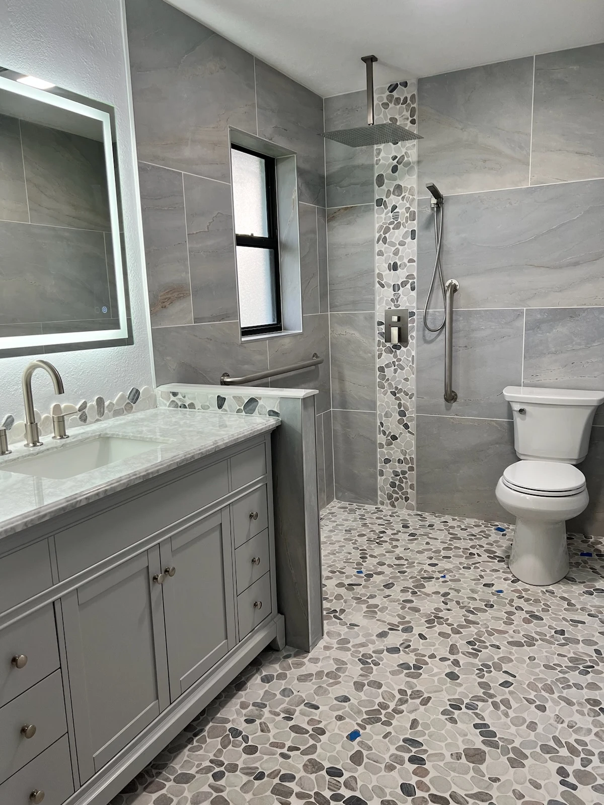 Bathroom with a gray vanity, open tiled shower, patterned floor and vertical accent strip.