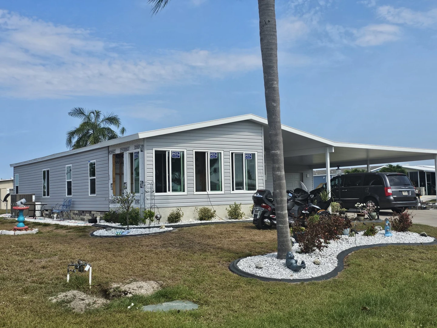 Light-sided home with a carport, windows and landscaped planting beds.