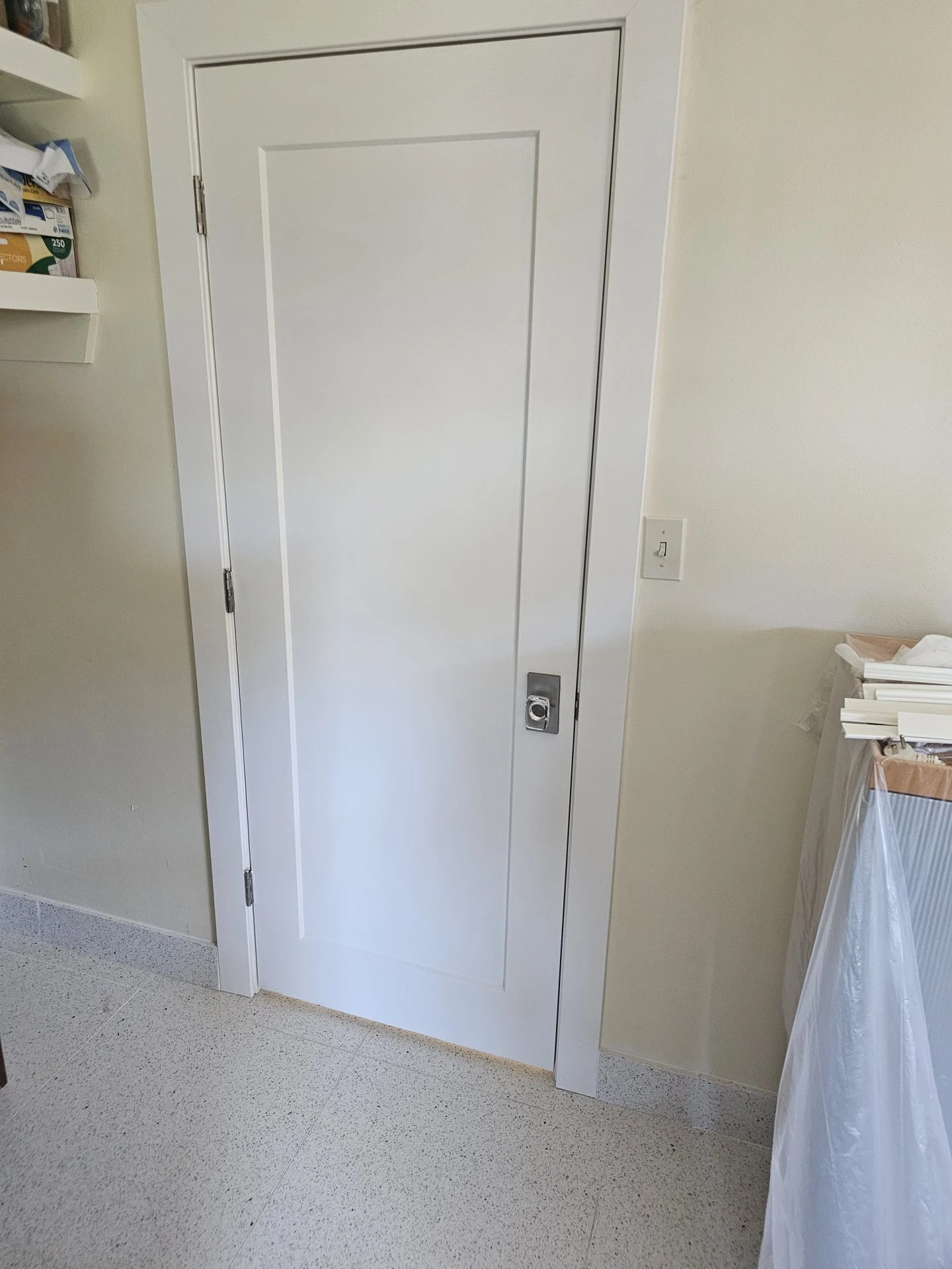 White paneled interior door, casing and baseboard during installation, with incomplete handle hardware.