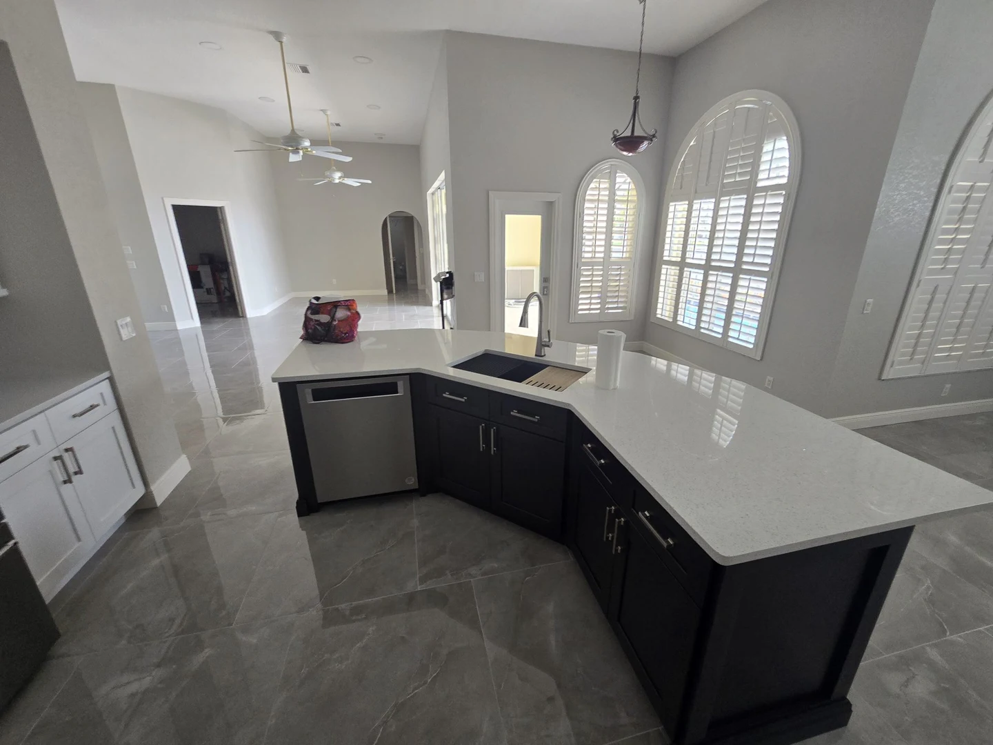 Dark kitchen island with a pale countertop, surrounded by arched windows and gray tile flooring.