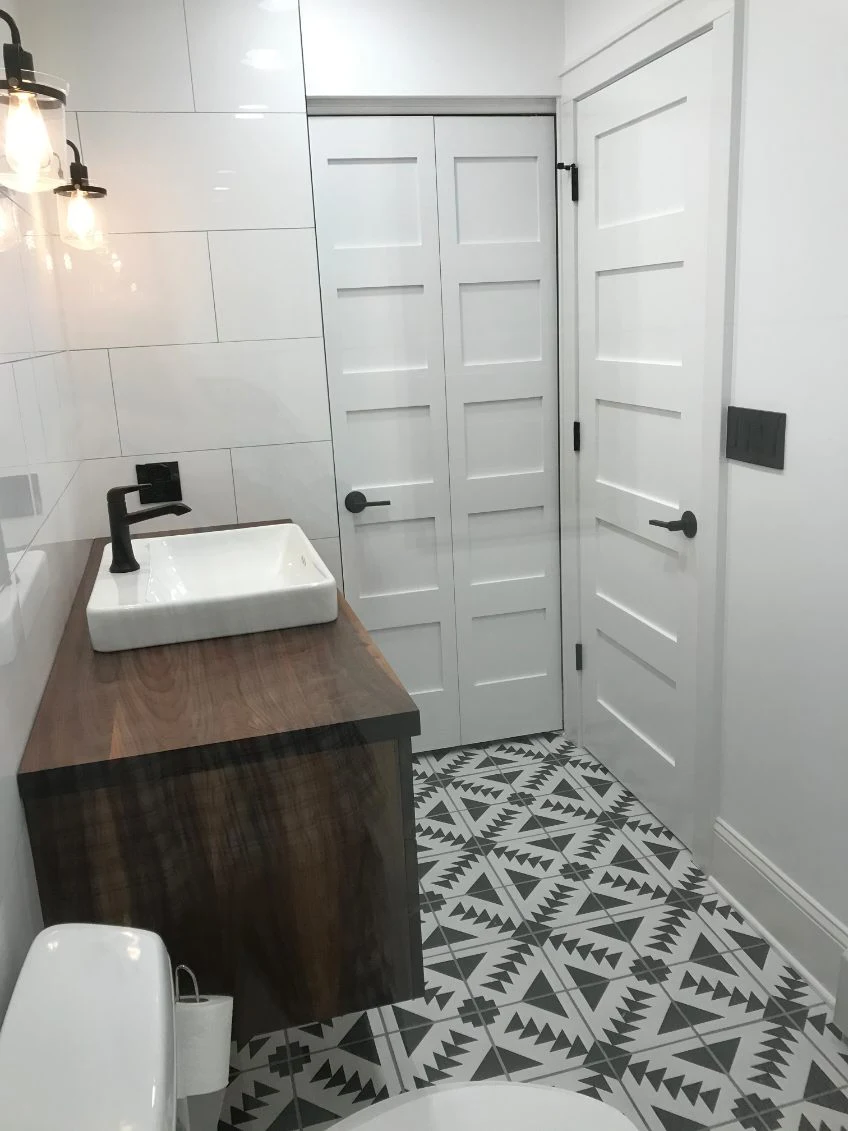 Bathroom with patterned black-and-white floor tile, a wood vanity and white paneled door.
