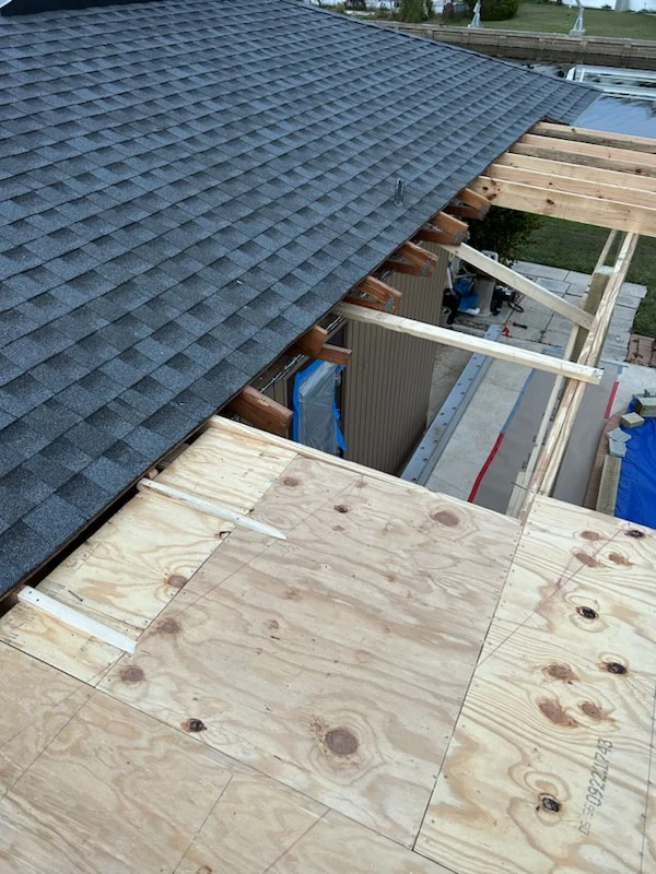 Exterior work in progress, showing exposed roof decking beside a shingled roof.