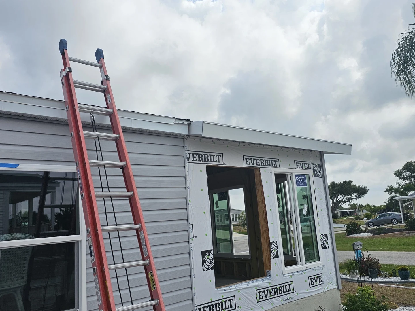 Window installation in progress, with a ladder, house wrap and exterior trim materials.